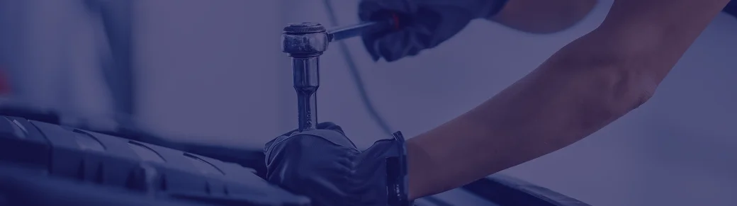 Un mécanicien serre un boulon sous le capot d'une voiture à l'aide d'une clé à cliquet. Ses mains gantées suggèrent concentration et précision dans un garage propre et bien éclairé